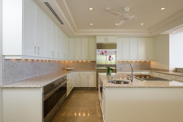 kitchen featuring white cabinetry, sink, stainless steel appliances, a raised ceiling, and light stone counters