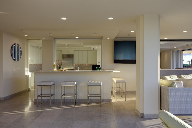 kitchen featuring a kitchen breakfast bar, tasteful backsplash, stainless steel built in fridge, and white cabinetry