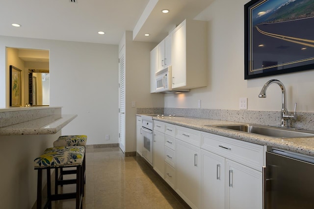 kitchen with white cabinetry, light stone countertops, white appliances, and sink