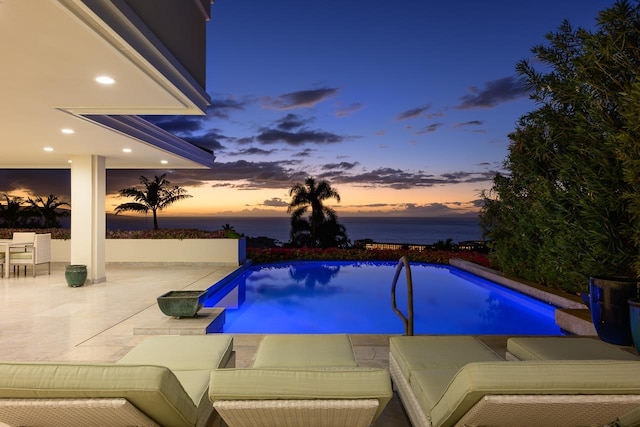 pool at dusk with a water view and a patio