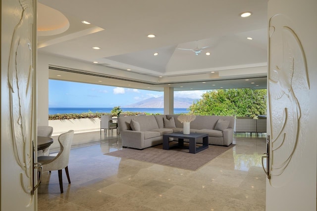 living room featuring lofted ceiling, a water view, ceiling fan, and a tray ceiling