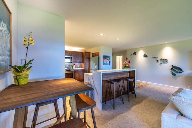 kitchen with carpet floors, stainless steel appliances, backsplash, kitchen peninsula, and a breakfast bar area