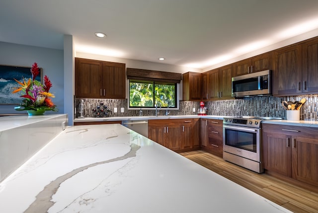 kitchen featuring tasteful backsplash, sink, light hardwood / wood-style flooring, stainless steel appliances, and light stone counters