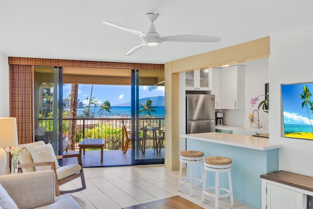 kitchen with a sink, a kitchen breakfast bar, white cabinetry, freestanding refrigerator, and glass insert cabinets