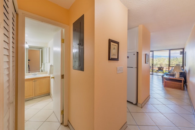 corridor with electric panel, a wall of windows, a textured ceiling, a sink, and light tile patterned flooring