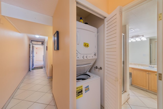 laundry area with light tile patterned floors, laundry area, stacked washing maching and dryer, and a sink