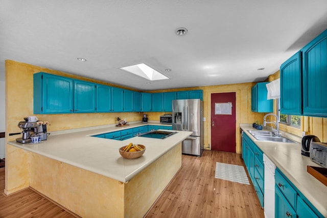 kitchen featuring a sink, appliances with stainless steel finishes, light wood finished floors, a skylight, and blue cabinets