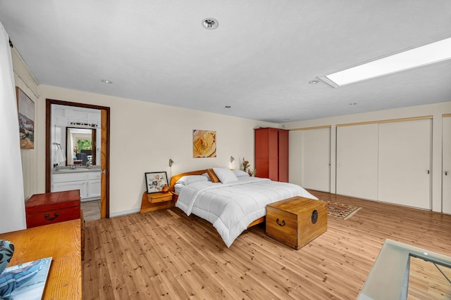 bedroom featuring light wood-style flooring, a skylight, recessed lighting, and multiple closets