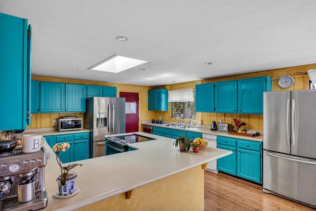kitchen featuring a skylight, light wood-type flooring, light countertops, and appliances with stainless steel finishes