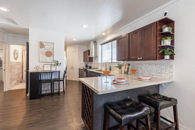 kitchen with open shelves, a sink, a breakfast bar area, wall chimney range hood, and light countertops