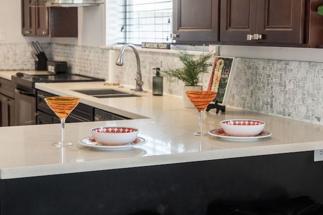 kitchen featuring a sink, decorative backsplash, light countertops, black electric range, and dark brown cabinets