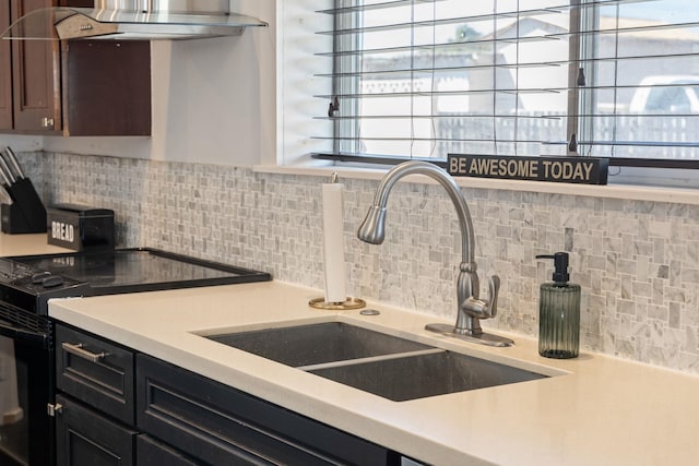 kitchen featuring tasteful backsplash, wall chimney range hood, light countertops, black / electric stove, and a sink