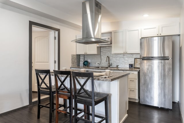 kitchen with backsplash, dark wood-type flooring, a kitchen breakfast bar, island exhaust hood, and freestanding refrigerator