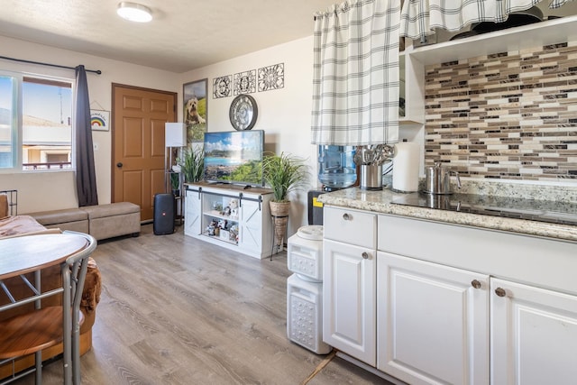 kitchen featuring light stone counters, light wood finished floors, white cabinets, black electric stovetop, and tasteful backsplash