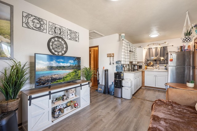 kitchen with light countertops, freestanding refrigerator, wood finished floors, white cabinetry, and a sink