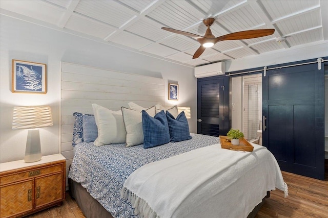 bedroom featuring a barn door, ceiling fan, an AC wall unit, and hardwood / wood-style floors