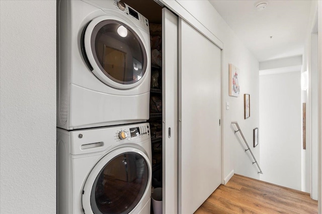 laundry area featuring stacked washer and clothes dryer and light wood-type flooring