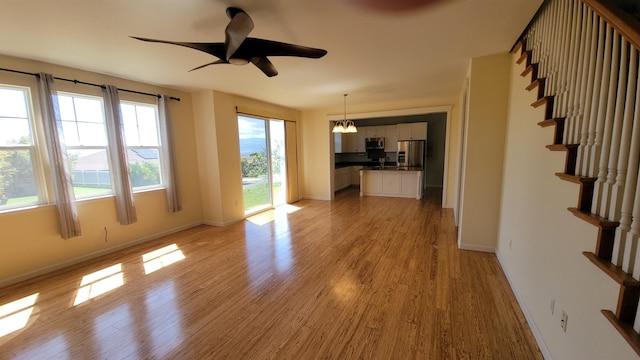 unfurnished living room with stairway, light wood-type flooring, and baseboards