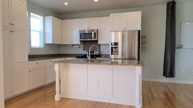 kitchen featuring stainless steel appliances, light wood-style floors, recessed lighting, an island with sink, and white cabinetry