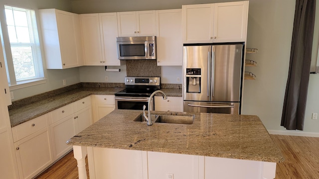 kitchen featuring stainless steel appliances, a sink, light wood-style floors, white cabinetry, and stone counters
