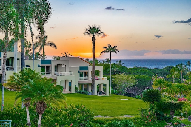 back house at dusk with a yard, a balcony, and a water view