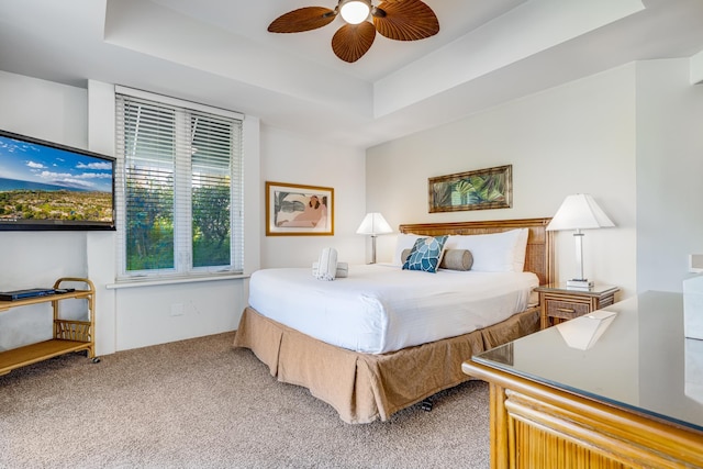 carpeted bedroom featuring ceiling fan and a tray ceiling