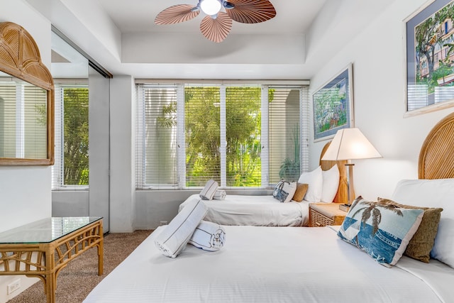 carpeted bedroom featuring ceiling fan and a raised ceiling