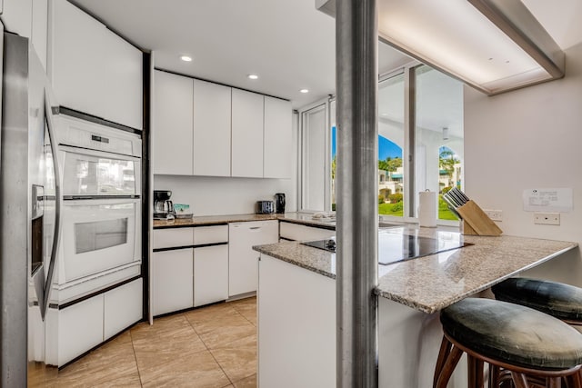 kitchen featuring light stone countertops, kitchen peninsula, white appliances, a breakfast bar, and white cabinets