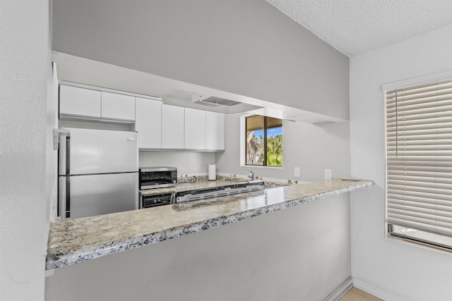 kitchen featuring kitchen peninsula, light stone countertops, a textured ceiling, stainless steel appliances, and white cabinets