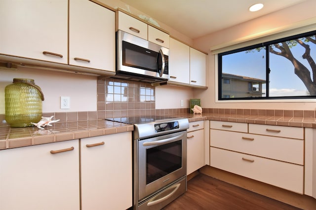 kitchen featuring white cabinetry, dark hardwood / wood-style flooring, backsplash, tile countertops, and appliances with stainless steel finishes