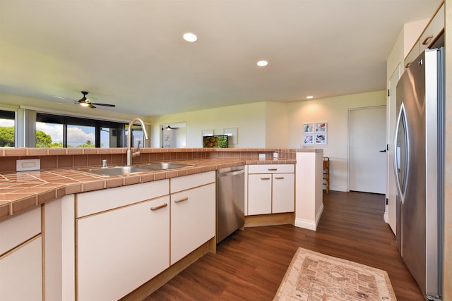 kitchen featuring sink, tile counters, kitchen peninsula, white cabinets, and appliances with stainless steel finishes