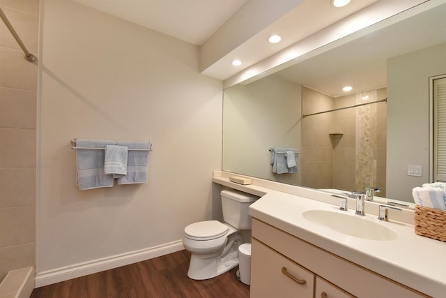 bathroom with a tile shower, hardwood / wood-style floors, vanity, and toilet