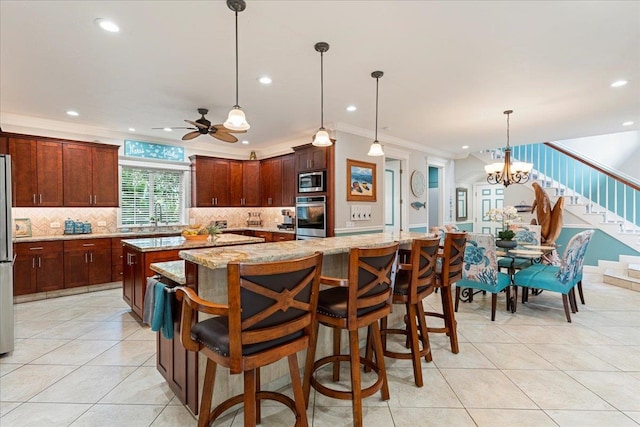 kitchen featuring a spacious island, stainless steel appliances, ornamental molding, light stone countertops, and decorative light fixtures