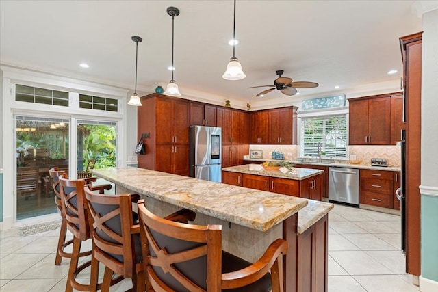 kitchen with appliances with stainless steel finishes, a kitchen island, a kitchen breakfast bar, pendant lighting, and crown molding