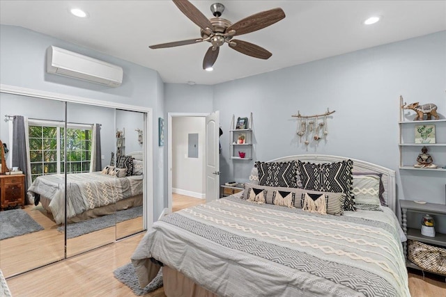 bedroom featuring light hardwood / wood-style flooring, a closet, ceiling fan, a wall unit AC, and electric panel