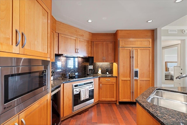 kitchen with tasteful backsplash, a sink, dark stone countertops, and built in appliances