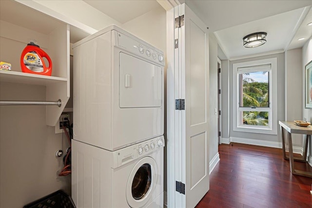 laundry room featuring stacked washer and dryer, dark wood finished floors, laundry area, and baseboards