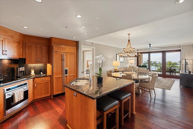 kitchen with black electric stovetop, brown cabinetry, open floor plan, a sink, and oven