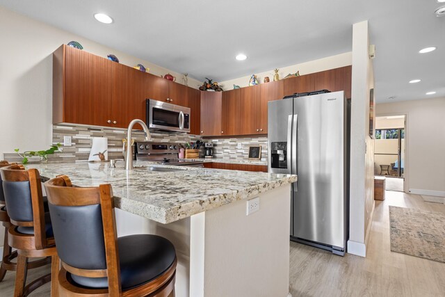 kitchen featuring stainless steel appliances, backsplash, kitchen peninsula, a breakfast bar, and light wood-type flooring