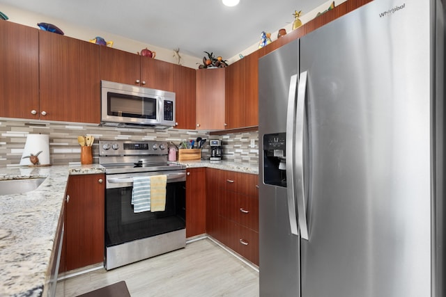 kitchen featuring backsplash, sink, light stone countertops, light hardwood / wood-style floors, and stainless steel appliances