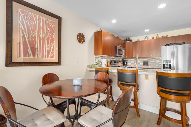 kitchen with kitchen peninsula, light wood-type flooring, backsplash, stainless steel appliances, and sink