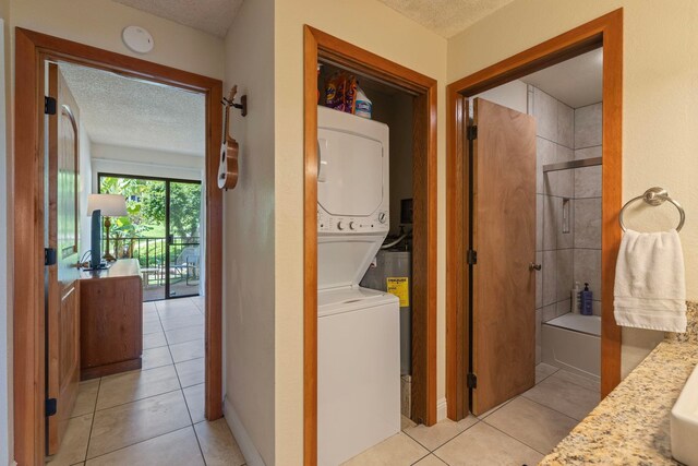 laundry area featuring a textured ceiling, light tile patterned floors, and stacked washer and dryer