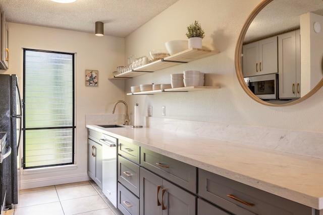 kitchen featuring a textured ceiling, light tile patterned floors, stainless steel appliances, sink, and gray cabinets