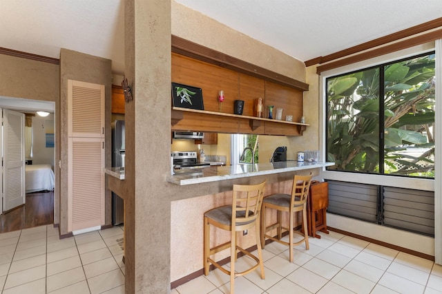 kitchen featuring stainless steel range with electric stovetop, light tile patterned floors, ornamental molding, a breakfast bar area, and extractor fan