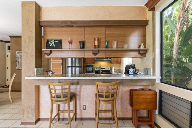 kitchen with a kitchen breakfast bar, stainless steel appliances, light tile patterned floors, and exhaust hood