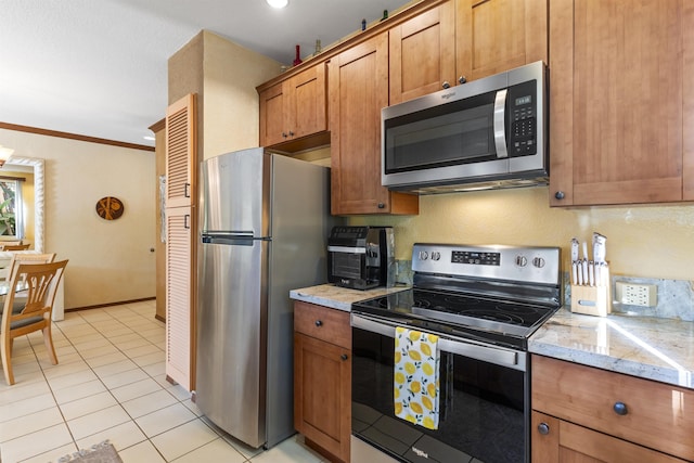 kitchen featuring light stone counters, light tile patterned flooring, stainless steel appliances, and ornamental molding