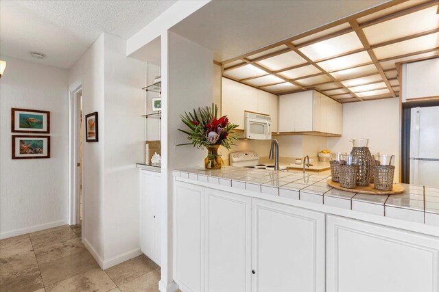 kitchen with white cabinetry, white appliances, baseboards, and tile counters