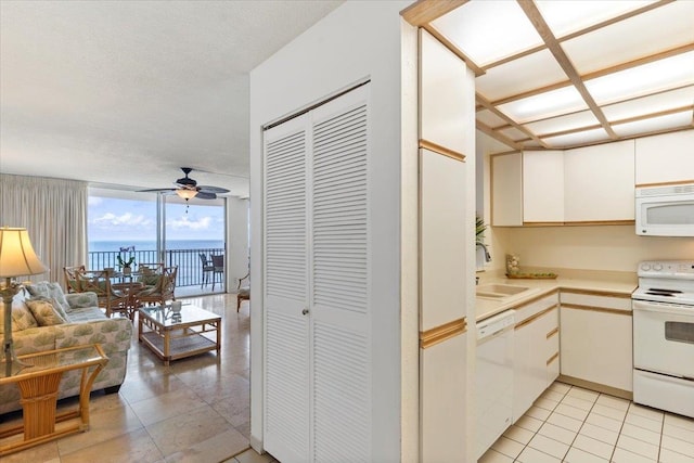 kitchen with white cabinetry, a wall of windows, a water view, white appliances, and ceiling fan