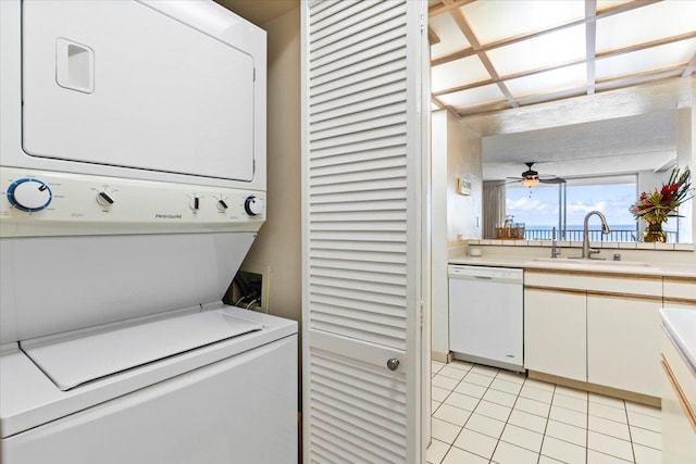 clothes washing area with light tile patterned flooring, ceiling fan, stacked washer / dryer, and sink