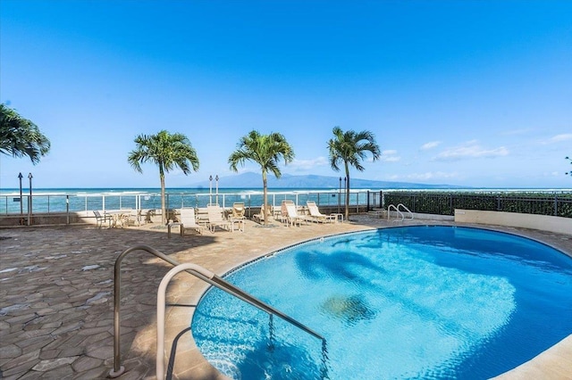community pool featuring fence, a water view, and a patio